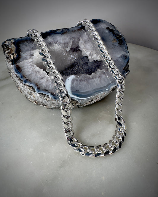 A sterling silver cuban link style chain displayed on a gray base, with a box clasp.