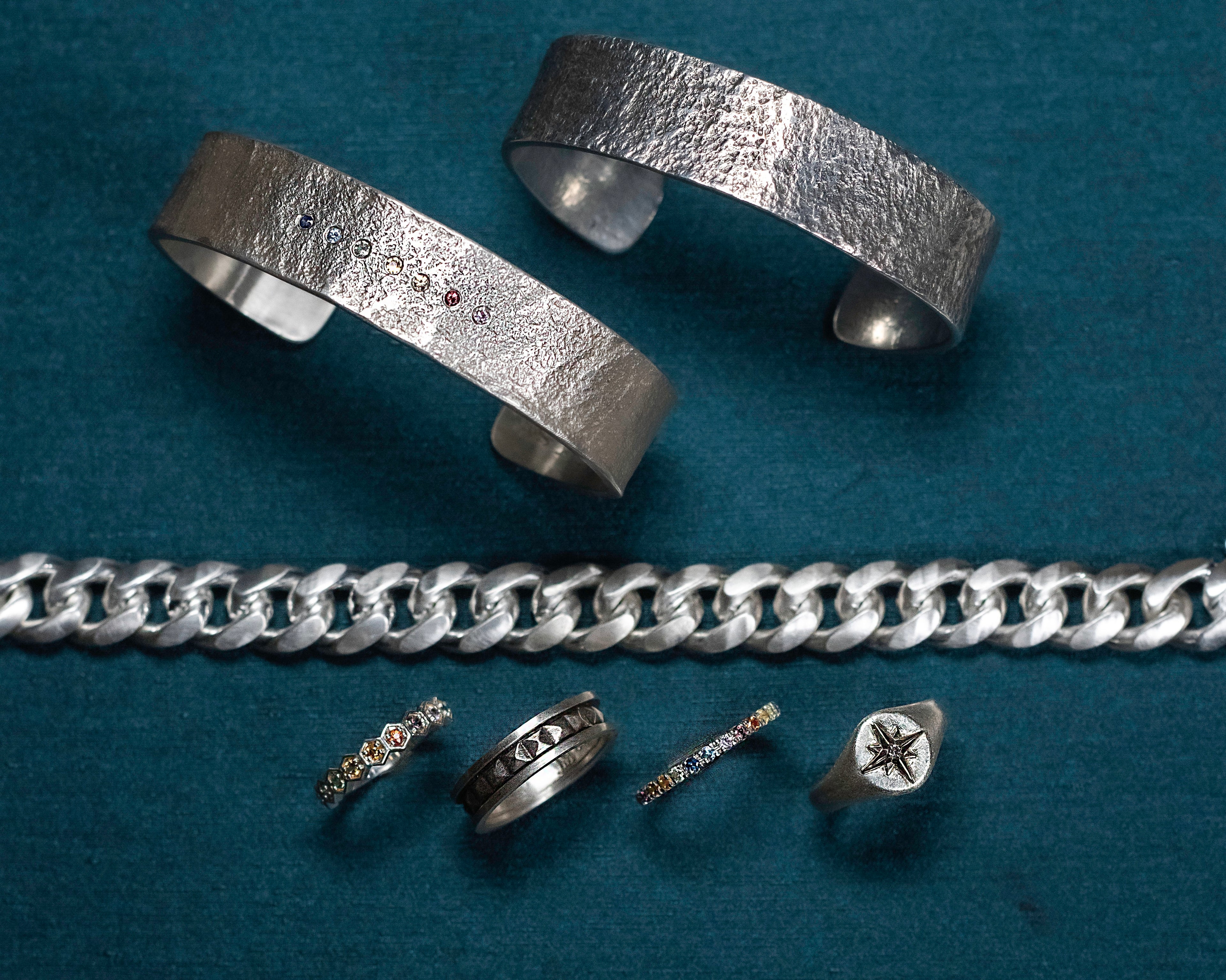 Collection of silver jewelry including bracelets and rings on a blue background
