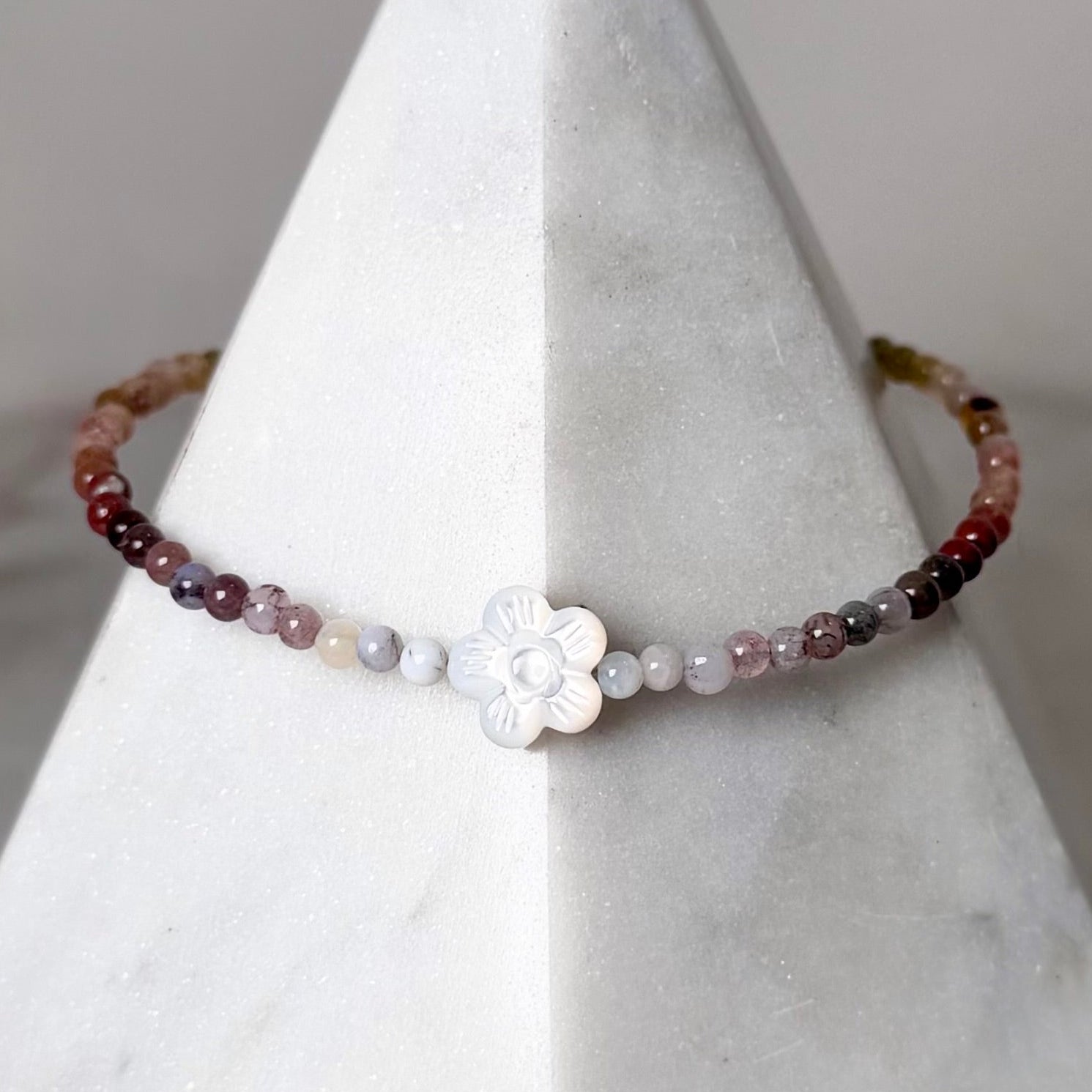 Beaded bracelet with a white flower charm on a gray stand