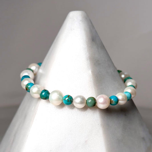Pearl and turquoise beaded bracelet on a white marble stand with a gray background